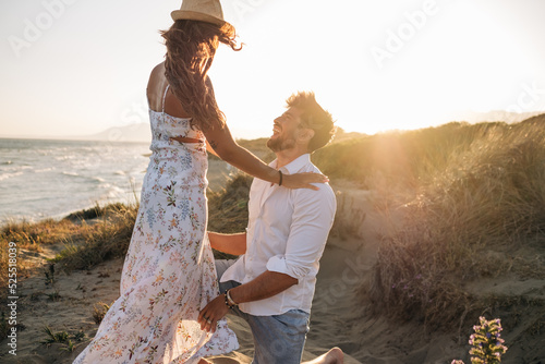 Boyfriend kneeling and making proposal to girlfriend on sunset beach photo