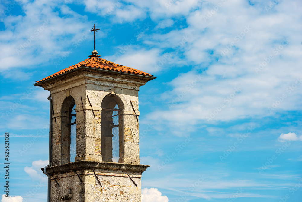 Ancient bell tower of a small church against a blue sky with clouds (Chiesa della Beata Vergine della Mercede or dell'Ancona), 1687. Spilimbergo, Pordenone, Friuli-Venezia Giulia, Italy, Europe.
