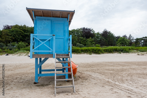 A blue lifeguard booth on the beach on a cloudy day. Orange lifeboat leaning against the side of the house.