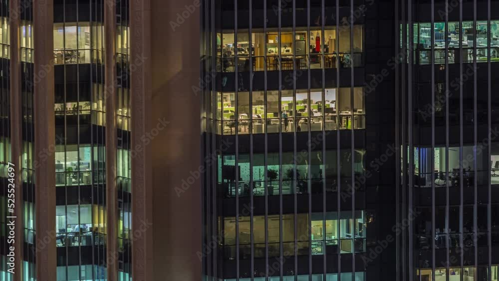 Windows lights in modern office buildings timelapse at night. Multi-level skyscrapers with illuminated open space rooms inside. People working at tables Windows lights in modern office buildings timelapse at night. Multi-level skyscrapers with illuminated open space rooms inside. People working at tables