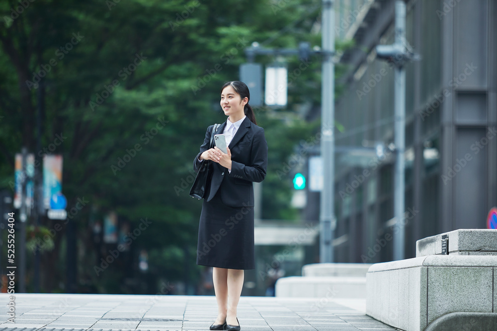 オフィス街でスーツを着てスマートフォンを持つ若い女性 オフィス街でスーツを着てスマートフォンを持つ若い女性
