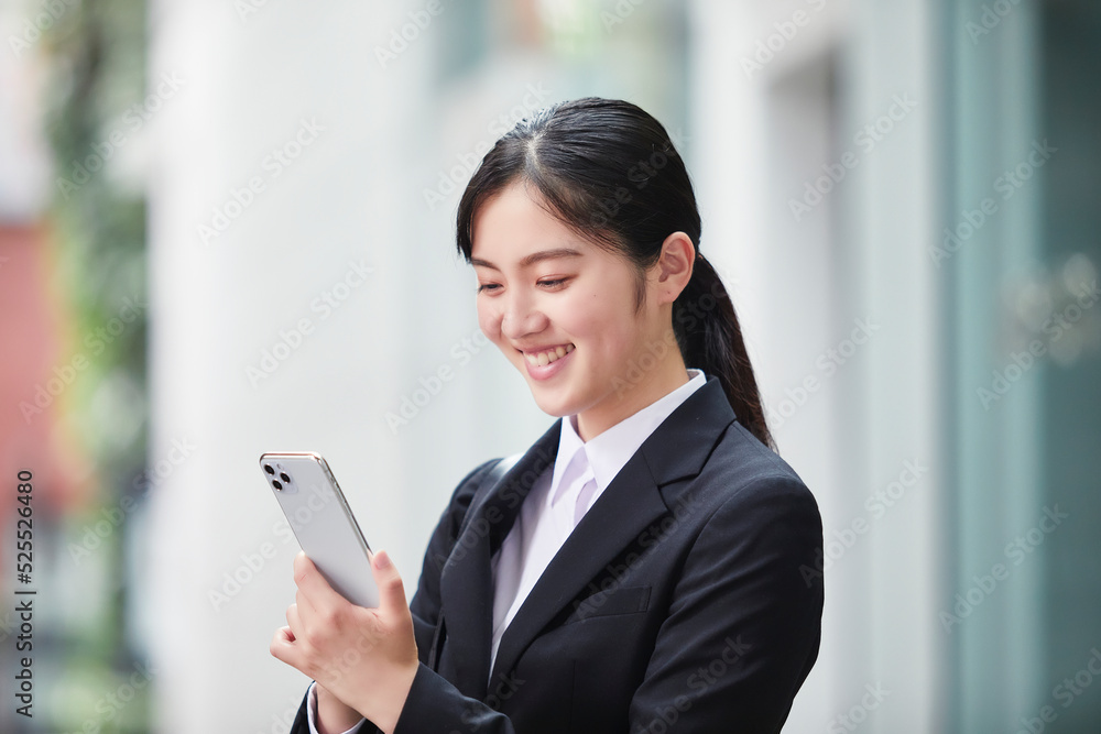オフィス街でスーツを着てスマートフォンを持つ若い女性 オフィス街でスーツを着てスマートフォンを持つ若い女性