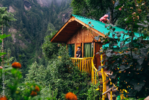 man on balcony of wooden treehouse hidden in the cedar forest of Jibhi mountains in North India