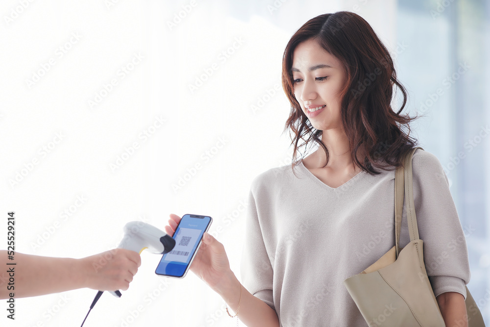 レジでスマートフォンを持ちキャッシュレス決済をする若い女性