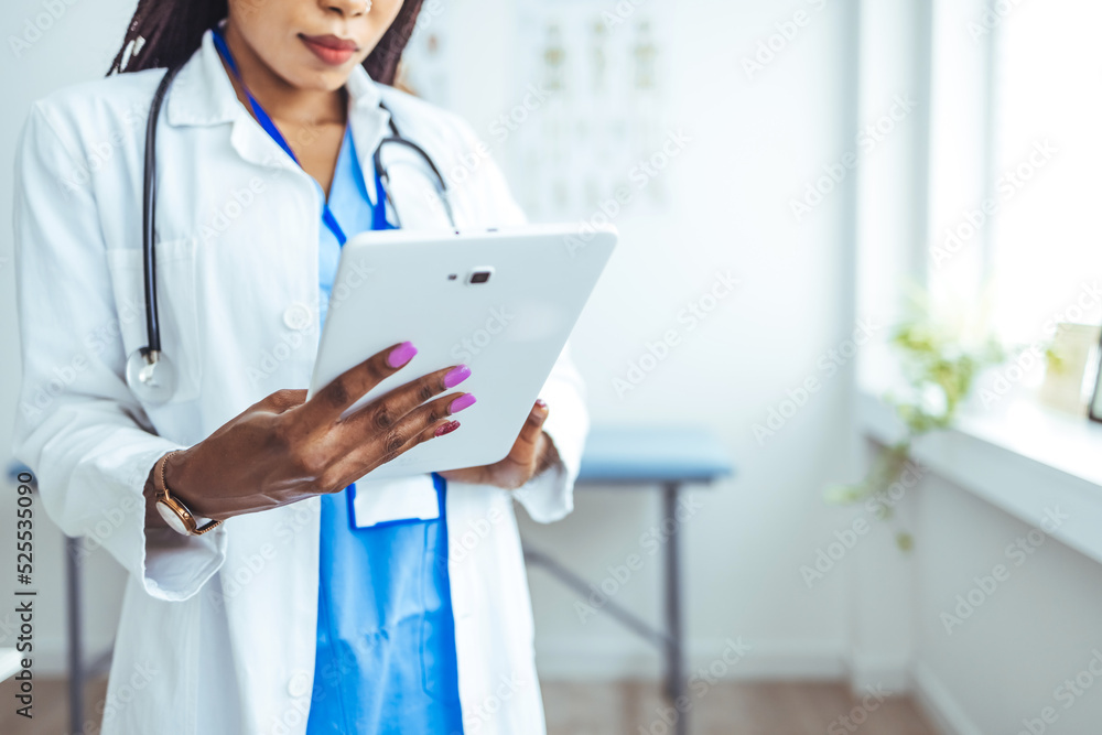 Shot of a young doctor using her digital tablet at work. Young female clinician in whitecoat and eyeglasses using touchpad while communicating with patients online. Doctor using digital tablet