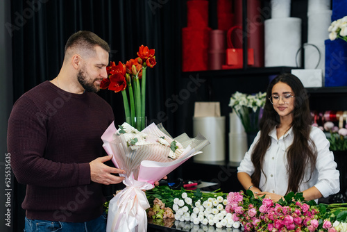 A young bearded man buys a beautiful bouquet of flowers for a girl's holiday in a cozy flower shop. Floristry and bouquet making in a flower shop. Small business.