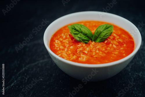 Fotografie Tomato soup with rice and basil in a white bowl on a dark stone table