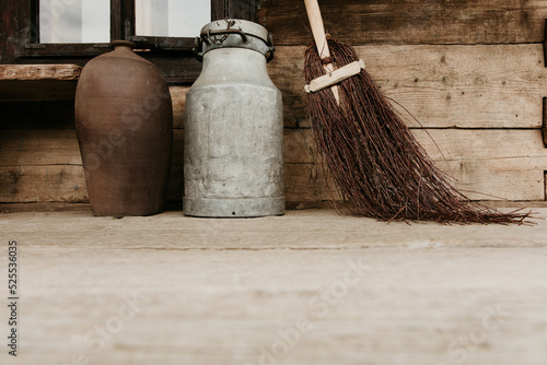 A brown ceramic vase, a vintage metal milk churn can and a rustic besom broom on a wooden porch. Low angle photo with copy space. Countryside home detail mockup. Rural life.  photo