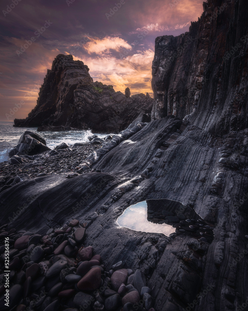 Sunrise over Black Church rock on the coast of Devon, UK. Beautiful morning landscape scene with the colourful cloudy sky over the rocky beach with the rock formation.