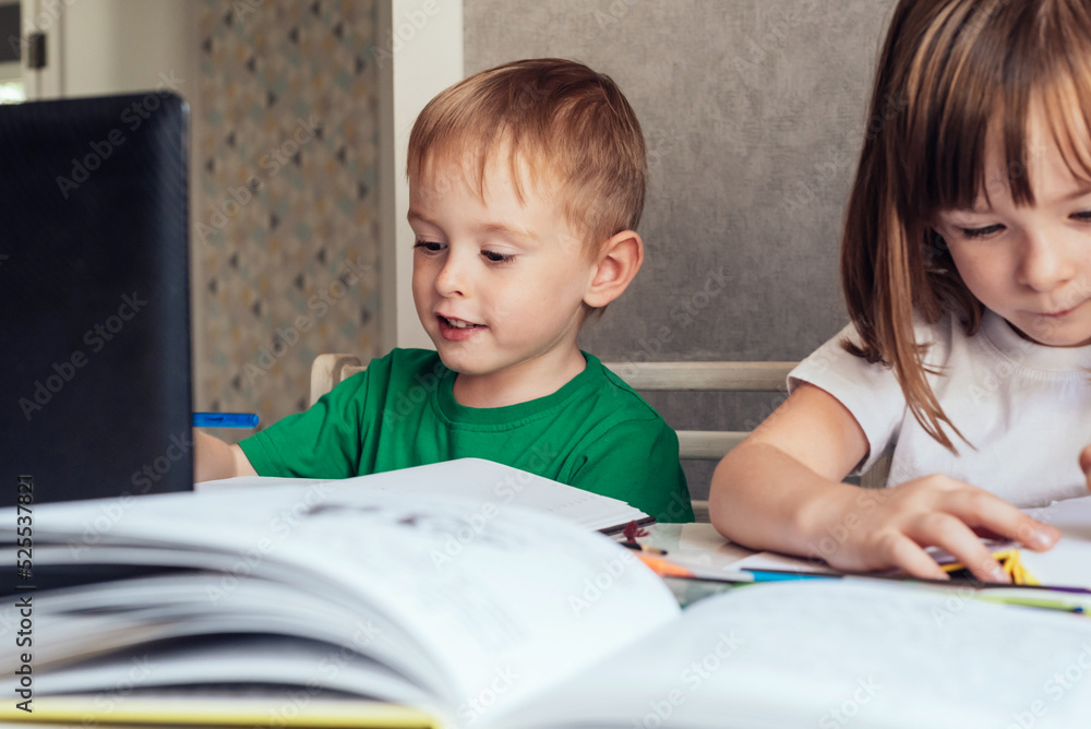 Child sits at the table, uses a laptop and writes in a notebook Child sits at the table, uses a laptop and writes in a notebook