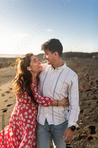 Romantic young ethnic couple cuddling on sandy seashore on sunny day