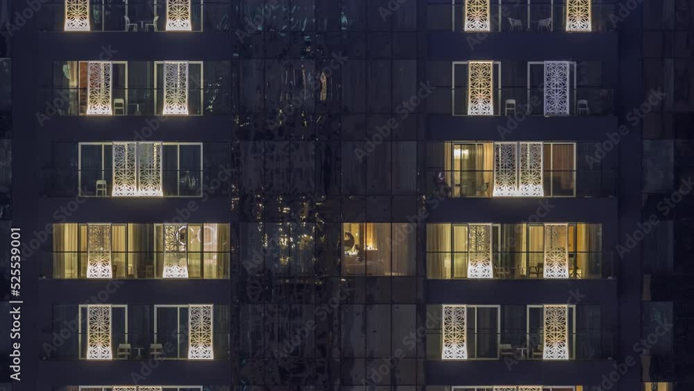 Windows lights in modern office and residential buildings timelapse at night. Multi-level skyscrapers with illuminated rooms inside. Some chairs on balconies