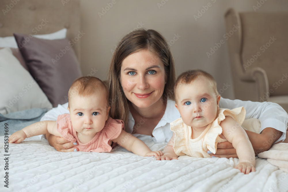Close-up portait of happy lovely young mother with two litlle twin sisters in casual clothes lying on bed with cotton linen Close-up portait of happy lovely young mother with two litlle twin sisters in casual clothes lying on bed with cotton linen