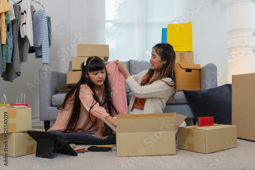 Mother and daughther as team working from home social live chat online sale business via computer tablet pc and show sample cloth and size meassurement before packing to the box and seal adhesive tape photo