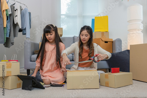 Mother and daughther as team working from home social live chat online sale business via computer tablet pc and show sample cloth and size meassurement before packing to the box and seal adhesive tape photo