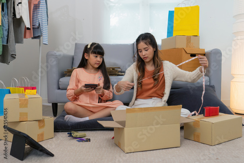 Mother and daughther as team working from home social live chat online sale business via computer tablet pc and show sample cloth and size meassurement before packing to the box and seal adhesive tape photo