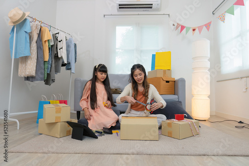 Mother and daughther as team working from home social live chat online sale business via computer tablet pc and show sample cloth and size meassurement before packing to the box and seal adhesive tape photo