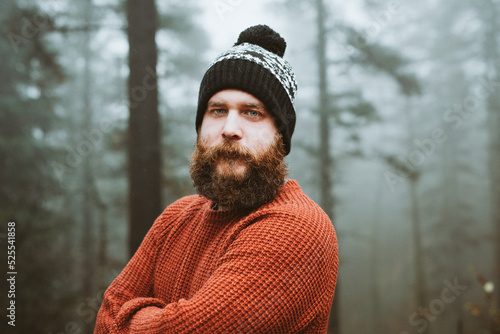 Bearded guy in sweater and hat near fir trees photo