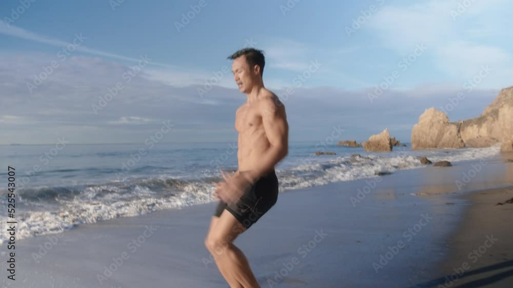 Fit and athletic young asian american man train and exercise on epic empty beach. Jogging on the spot, perform moves after online in app training program Fit and athletic young asian american man train and exercise on epic empty beach. Jogging on the spot, perform moves after online in app training program