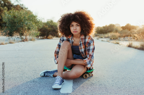 African American woman sitting on penny board on the asphalt road photo