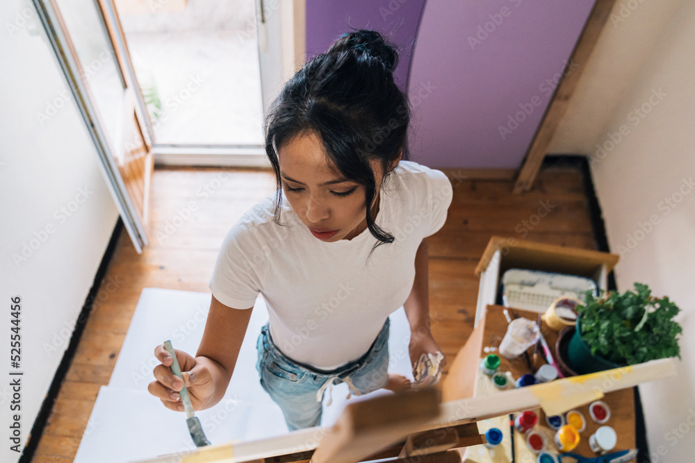 Young ethnic woman painting on canvas with brush Young ethnic woman painting on canvas with brush