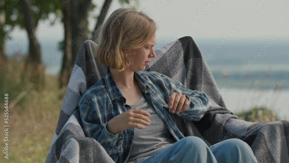 Young adult woman waving hands trying to catch annoying fly in front of her face sitting on camping chair outdoors.