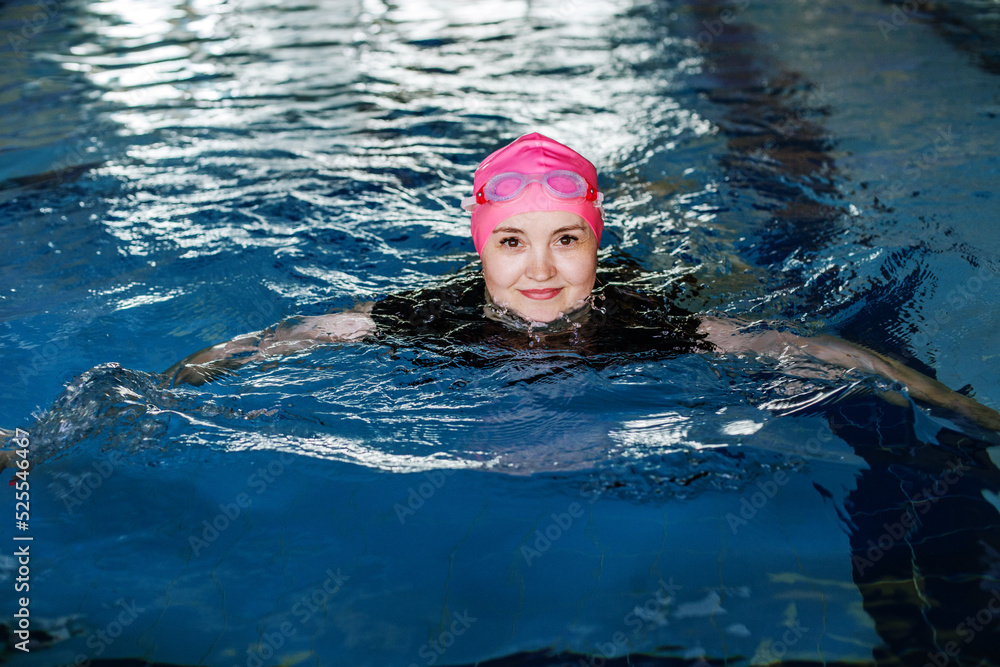 Woman swims in swimming pool. Goggles and swimming cap. Concept of sports and healthy lifestyle