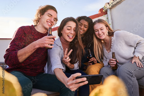 Joyful diverse friends taking selfie during party on terrace photo