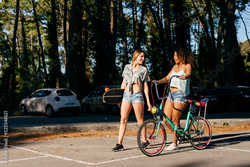 Female friends walking on street holding skate board and bicycle photo