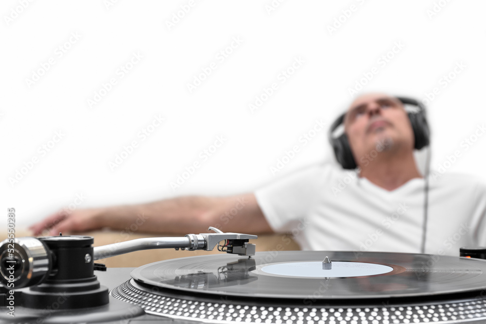 Vinyl record on the player against the background of a blurred man in headphones relaxing and listening to music.