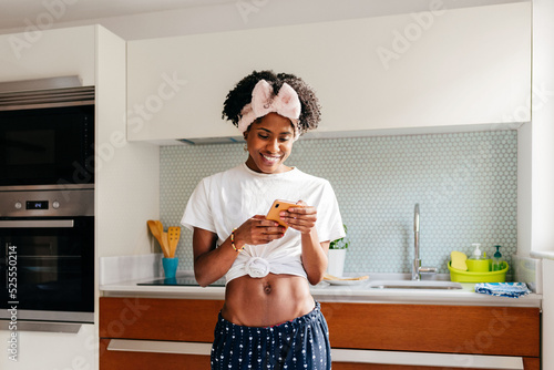 Cheerful black woman using smartphone in kitchen photo