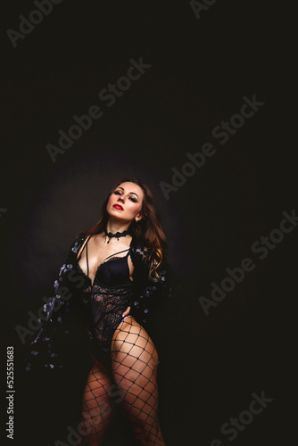 Woman in stage black costume posing and looking at camera on black background. Pretty lady with stage makeup and long curly hair. Concept beauty and fashion. Copy space, text place