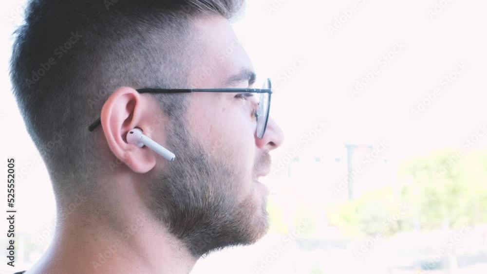 Using ear buds, young brown haired teen man using ear buds. Talking to phone by wearing wireless ear buds. Speaking and listening. Over shoulder view footage of young male using in-ear headphones. Using ear buds, young brown haired teen man using ear buds. Talking to phone by wearing wireless ear buds. Speaking and listening. Over shoulder view footage of young male using in-ear headphones.