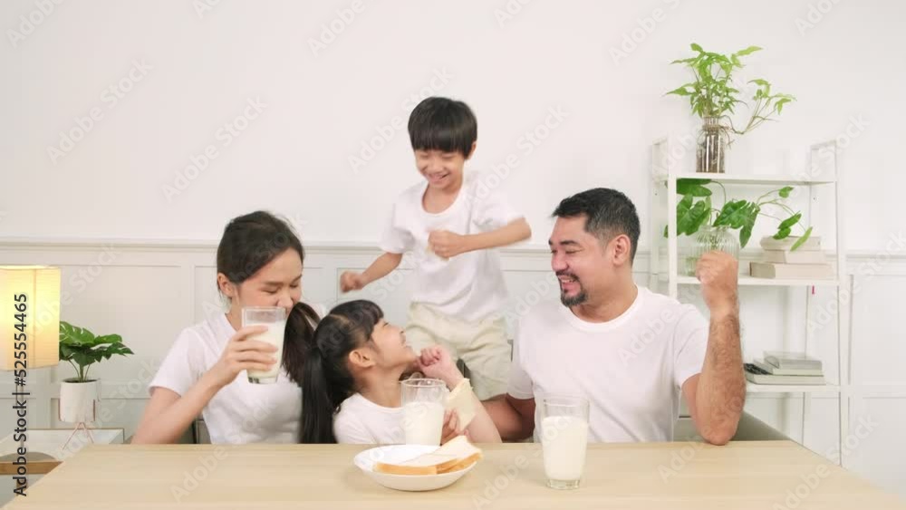 A Healthy Asian Thai family, little children, and young parents drink fresh white milk in glass and bread joy together at a dining table in morning, wellness nutrition home breakfast meal lifestyle. A Healthy Asian Thai family, little children, and young parents drink fresh white milk in glass and bread joy together at a dining table in morning, wellness nutrition home breakfast meal lifestyle.