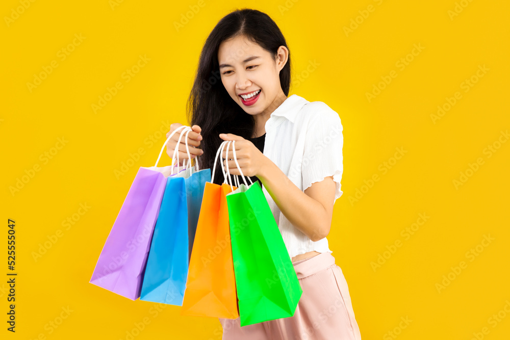 Young asian woman long hair style in black and white costume carrying the colorful paper shopping bags on yellow background.