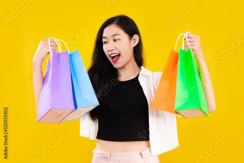 Young asian woman long hair style in black and white costume carrying and showing the colorful paper shopping bags on yellow background.