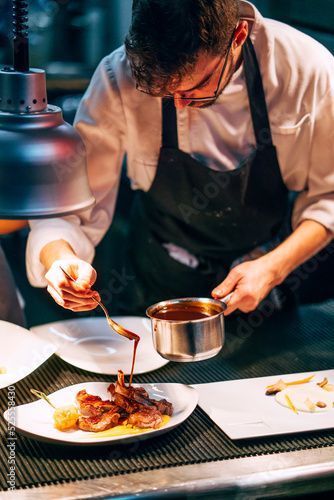 Professional chef pouring sauce on served meat