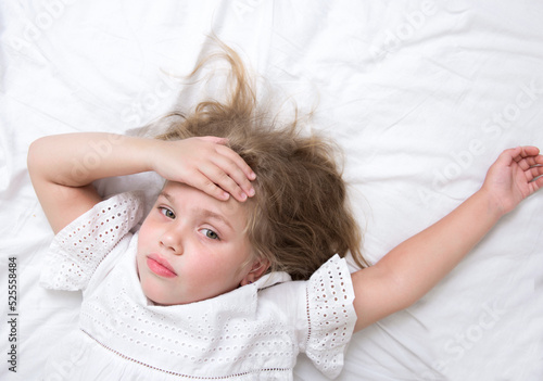 Child lying in bed with headache.Kid with head at forehead.Little caucasian girl with temperature, illness concept.