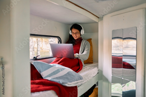 A multicultural woman sits on a bed in a van and works on a laptop.