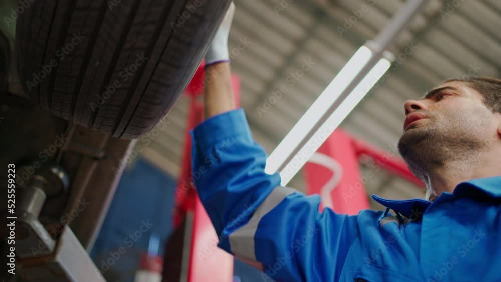 Professional car mechanic working on a vehicle in a service shop. Repairman using wearing glove check the tire and brake system in the workshop at garage. Maintenance and service concept Professional car mechanic working on a vehicle in a service shop. Repairman using wearing glove check the tire and brake system in the workshop at garage. Maintenance and service concept