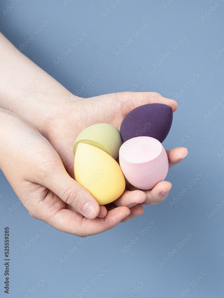 Woman holds group of soft sponges for makeup on blue background Woman holds group of soft sponges for makeup on blue background
