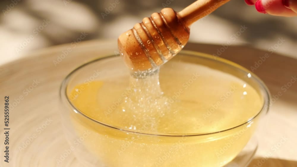 Honey dripping, pouring from honey dipper in a glass bowl. Close-up. Organic Thick honey dipping from the wooden honey spoon, closeup. 4K UHD video footage. Slow motion