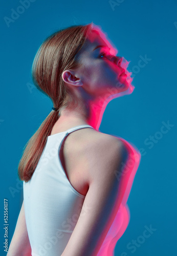 Art portrait of modern young caucasian girl in pink neon light on blue background. Long exposure. Nightlife, youth