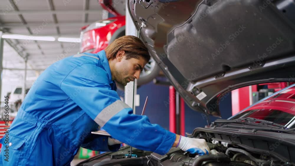Professional car mechanic in uniform working in a auto repair centers. Repairman using laptop to inspector the car engine system in the workshop at garage. Automobile engine inspector car damage Professional car mechanic in uniform working in a auto repair centers. Repairman using laptop to inspector the car engine system in the workshop at garage. Automobile engine inspector car damage