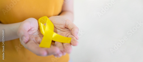 Young female holding yellow gold ribbon awareness symbol for endometriosis, suicide prevention, sarcoma bone cancer, bladder cancer, liver cancer and childhood cancer concept. Health care. Copy space.
