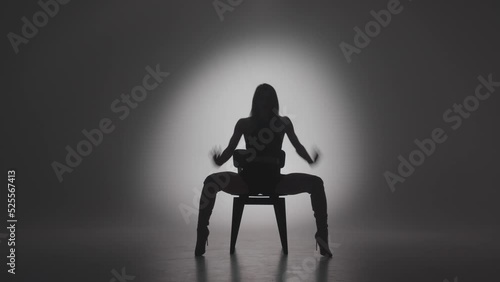 Dancing girl performs sexy movements on chair, silhouette of enticing woman in spotlight in studio. Vogue dance