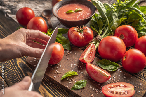 Hand is slicing ripe natural homemade tomatoes to make tomato basilic sauce. Rustic style