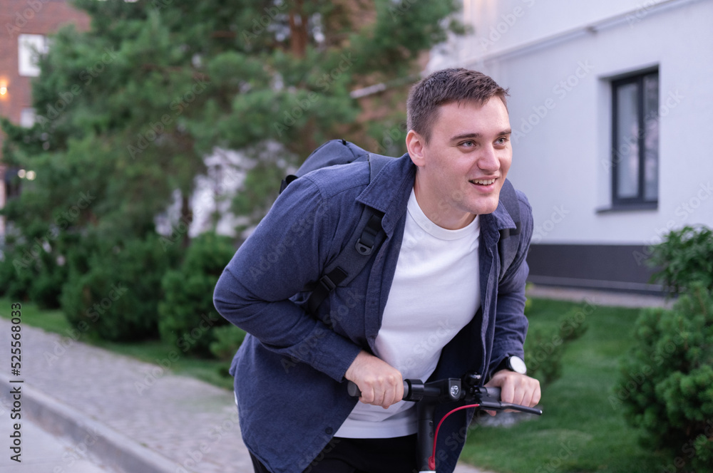 Obraz premium A businessman on an electric scooter rides through the park with a backpack. a man moves around the city on eco-friendly transport.