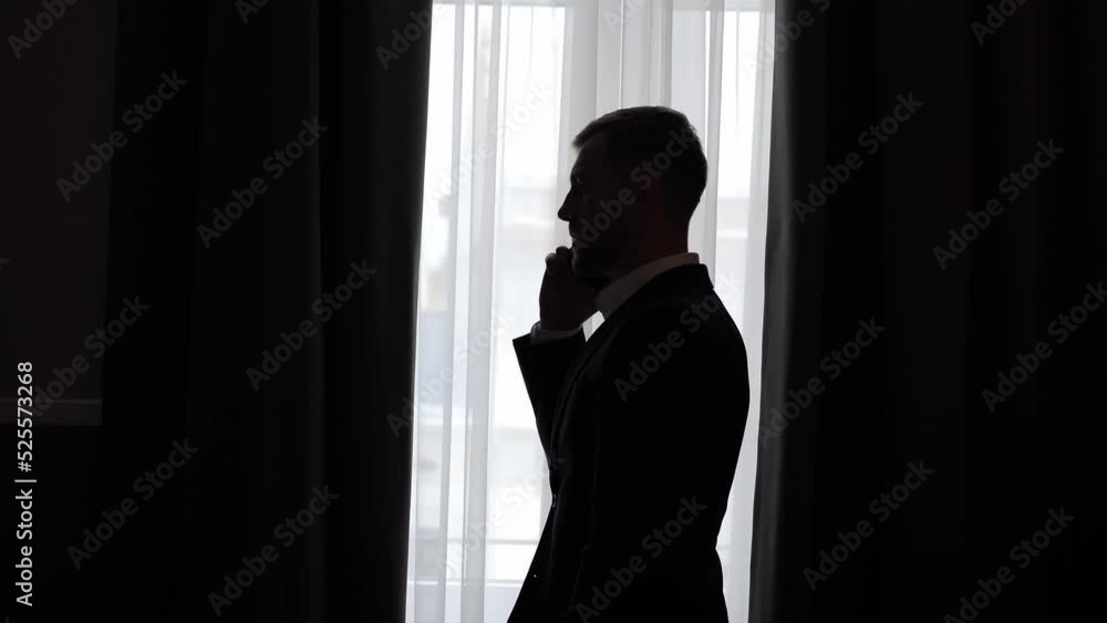 Silhouette of a business man standing near window talking on a mobile phone having phone conversation. Successful confident businessman making smartphone call. Private safety communication indoor. Silhouette of a business man standing near window talking on a mobile phone having phone conversation. Successful confident businessman making smartphone call. Private safety communication indoor.