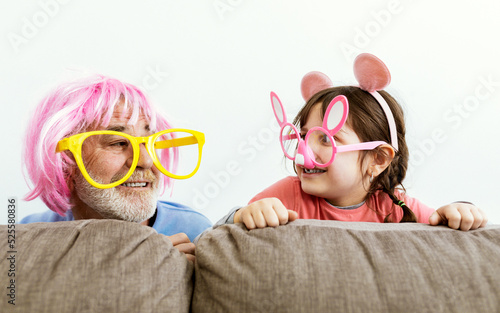 Happy girl playing with grandfather with fake glasses in room